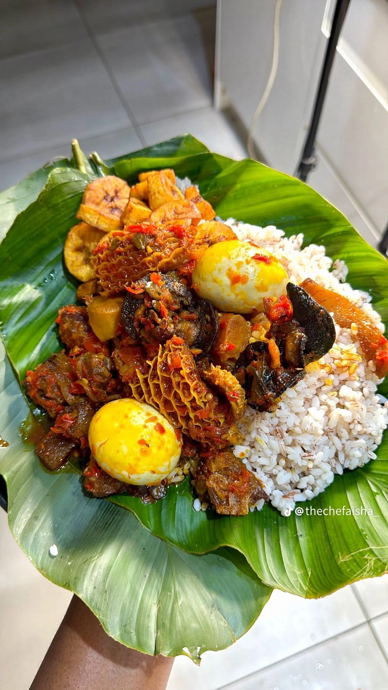 Ofada rice, pepper sauce, eggs and golden plantain on a leaf-lined plate