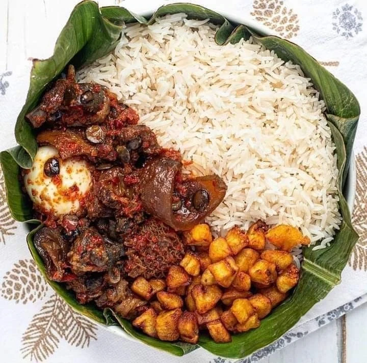 White rice with sauced beef, fried plantain and an egg on a leaf-lined plate