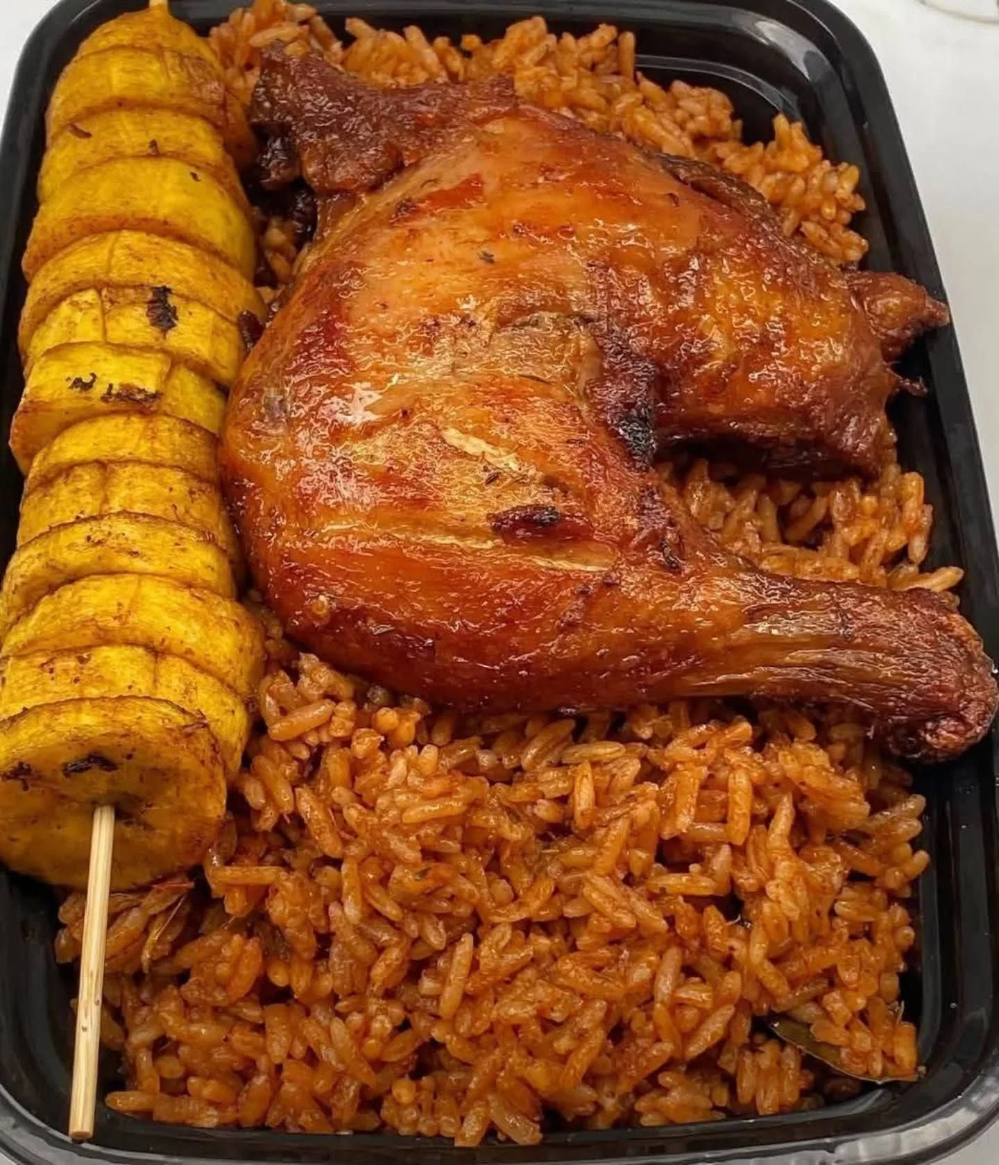 Jollof rice with chicken and fried plantain in a takeaway tray