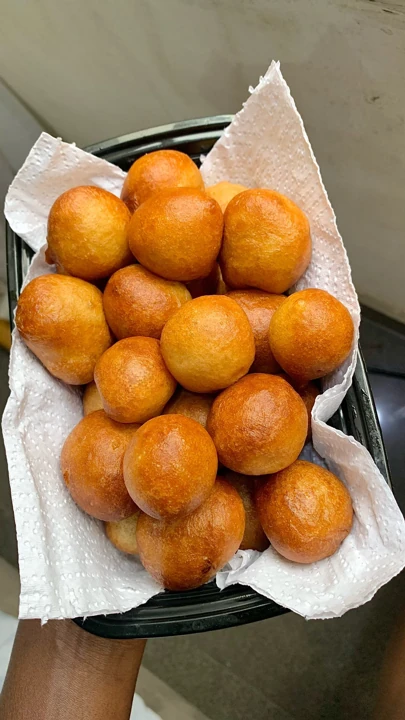Fresh golden puff-puff in a paper-lined takeaway bowl